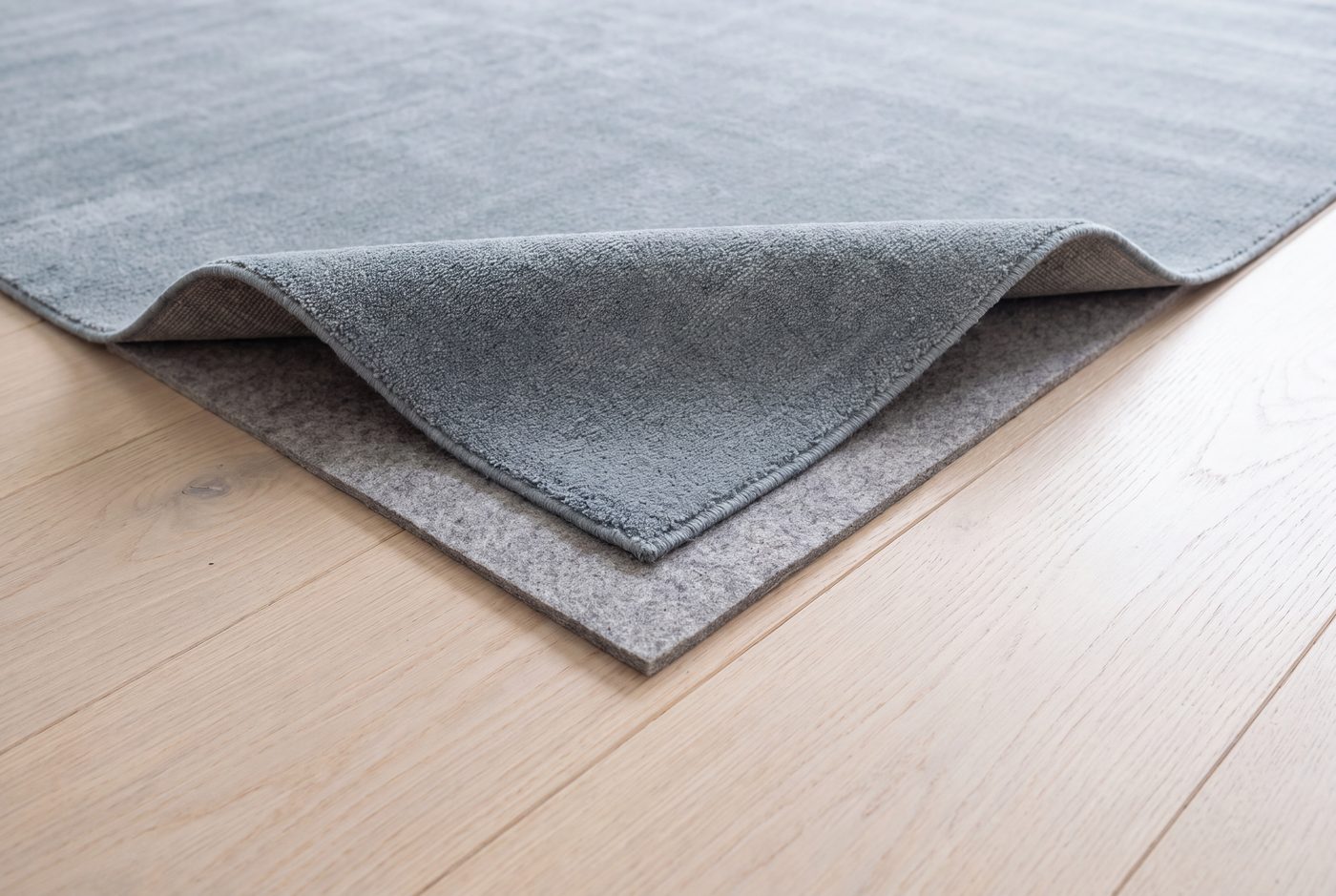A rug corner folded back to show the felt pad cut smaller than the rug