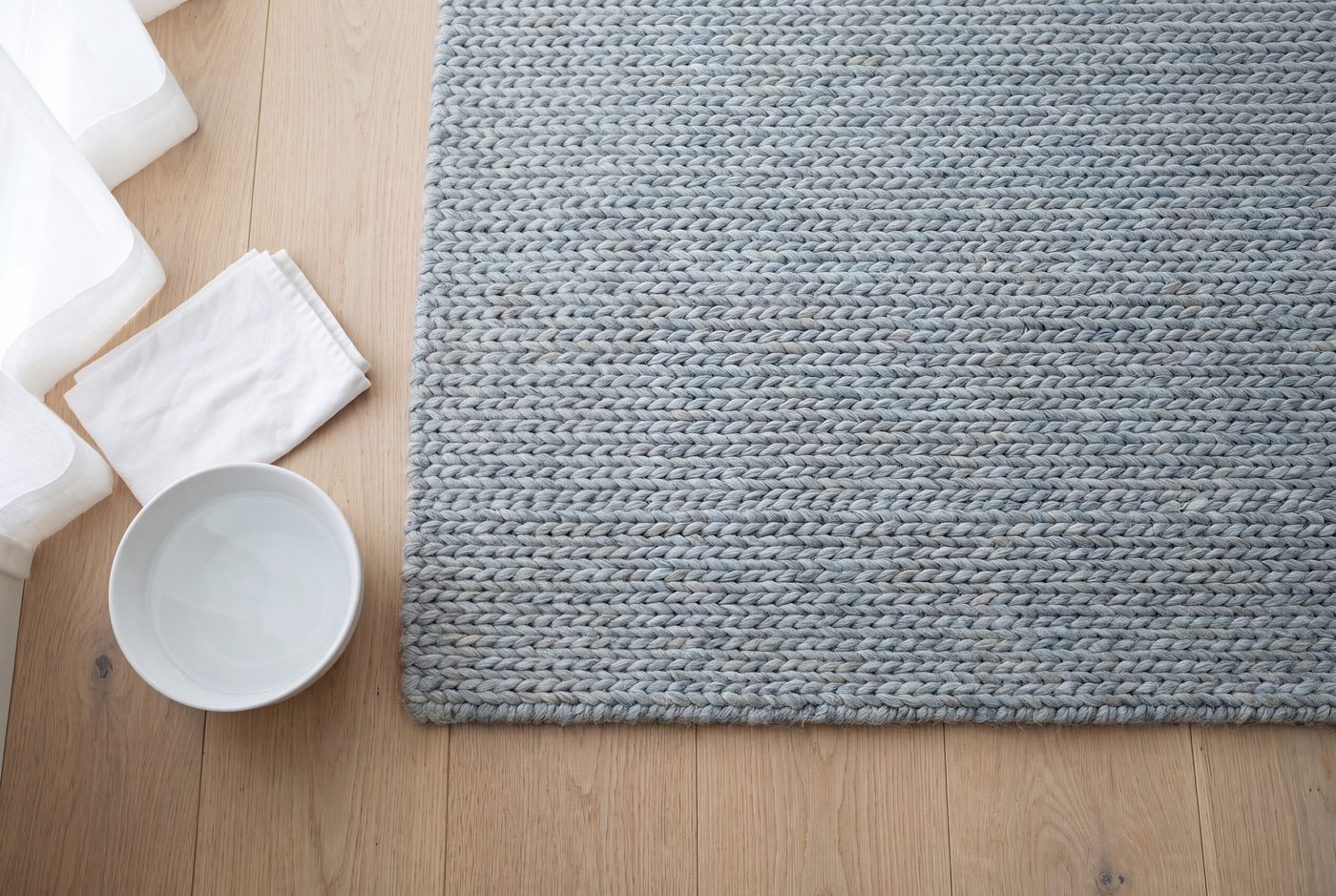 Close up of a woven wool rug beside a folded white cloth and a bowl of water