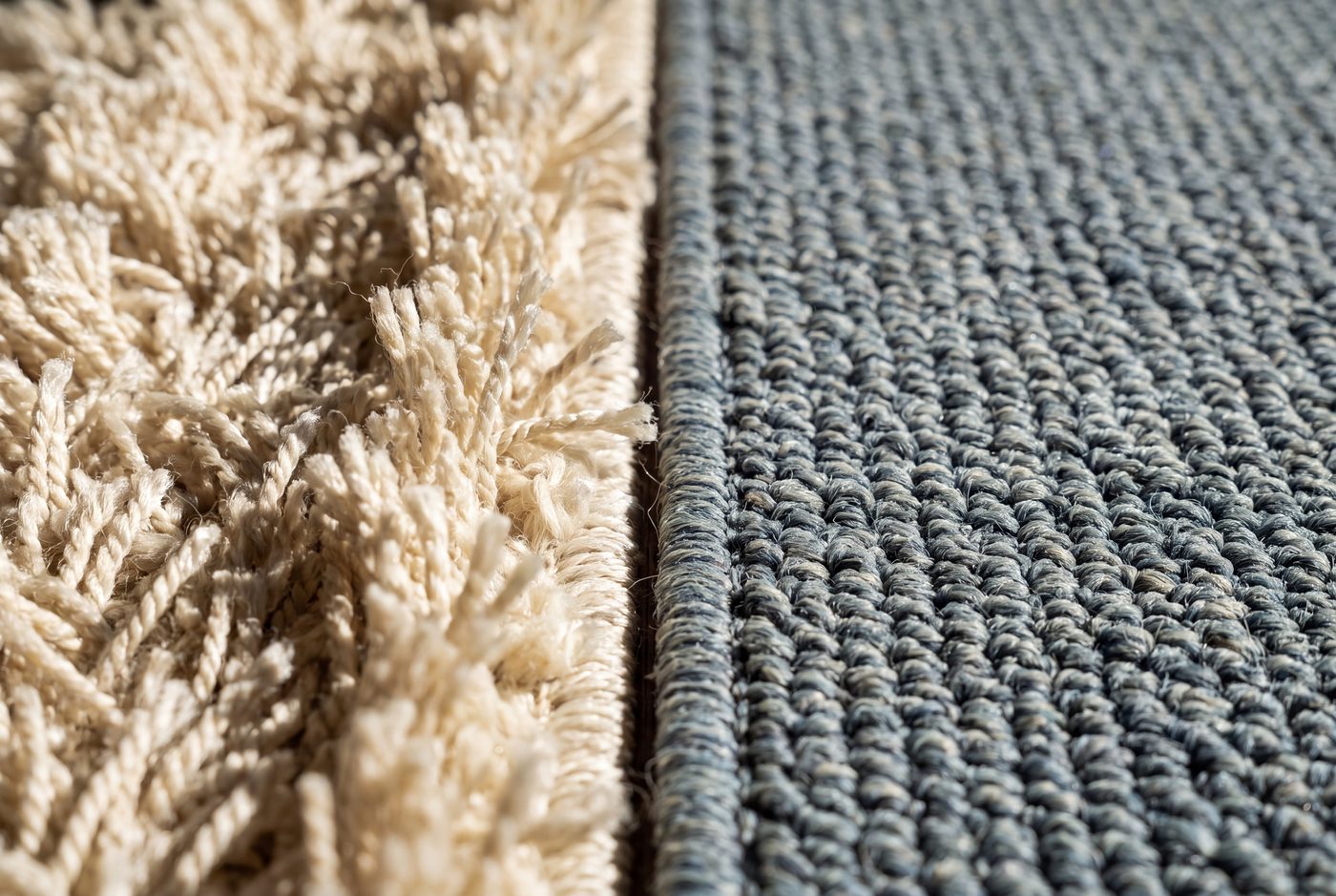 Two rugs butted edge to edge under raking light: a deep shaggy ivory pile on the left, a tight flat blue-grey weave on the right, with the difference in height obvious at the seam.
